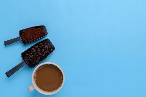 A top view of a Coffee mug, coffee beans, ground coffee on a blue background with a copy space
