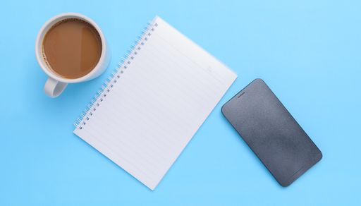 A top view of acoffee mug, book, smartphone on a blue background with a copy space