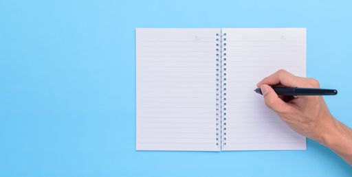 A top view of a Hand holding a pen to write on notebook on a blue background with a copy space