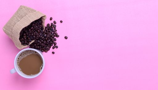 A top view of a Coffee mug and coffee beans on a pink background with a copy space