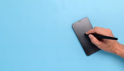 A top view of a hand Using a pen to write on your smartphone on a blue background with a copy space