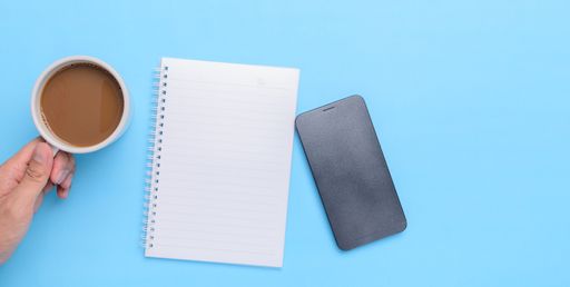 A top view of a coffee mug, book, smartphone on a blue background with a copy space