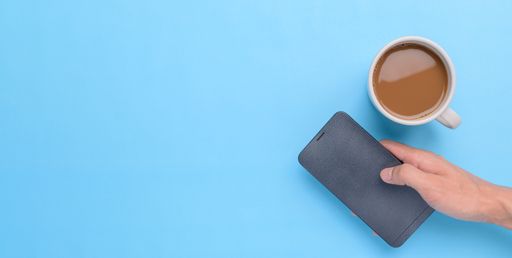 A top view of a Hand holding smartphone and coffee cup on blue background with a copy space