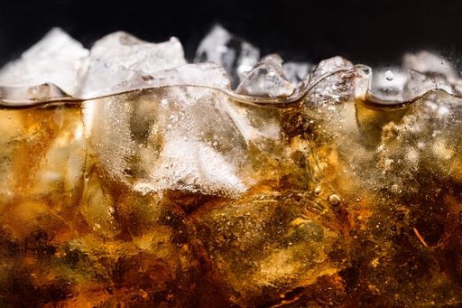 A close up of Cola in glass with clear ice cubes