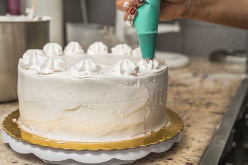 A closeup shot of a female pastry chef garnishing a white cake with cream using a piping bag