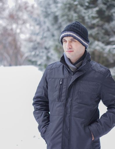 A vertical shot of a young male in a field covered in the snow under the sunlight in winter