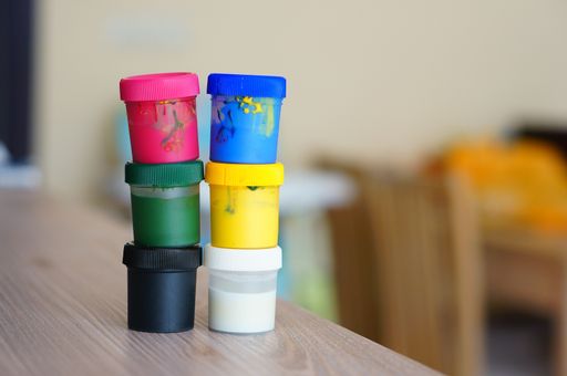 A closeup of colourful gouache paints in plastic jars on each other on the table under the lights