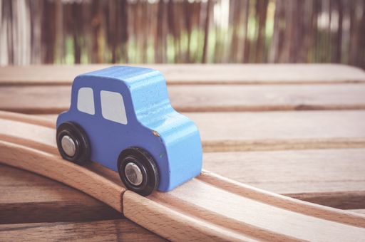 A closeup of a blue wooden toy car on the tracks under the lights with a blurry background