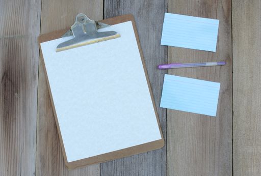 A clipboard with a blank sheet of paper on a flat wooden table background.