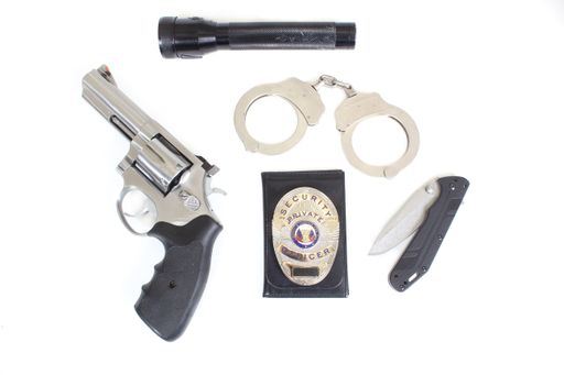A handgun, handcuffs, security badge, flashlight, and pocket knife isolated on a white background
