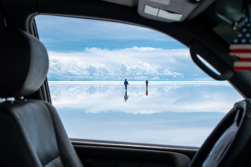 A view of people in Uyuni Desert, Bolivia with reflections of white clouds seen through a car window
