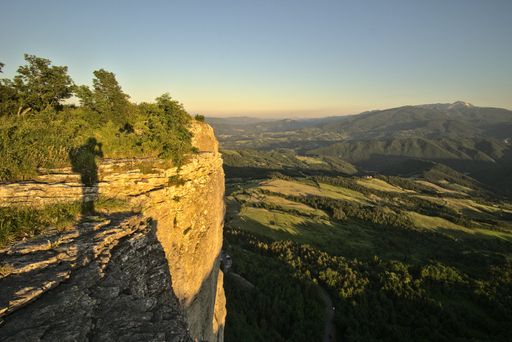 A long exposure shot of a cliff in the foreground, and natural landscapes in the background