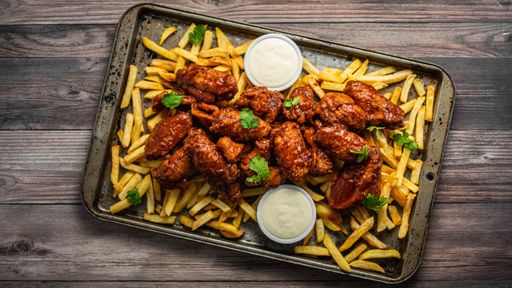 An overhead shot of buffalo wings with sauce and fries on a tray on wooden table