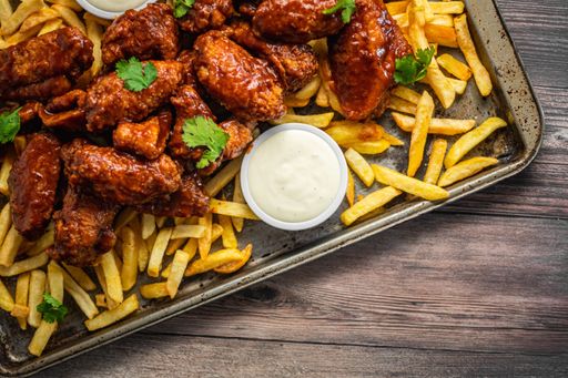 An overhead shot of buffalo wings with sauce and fries on a tray on wooden table