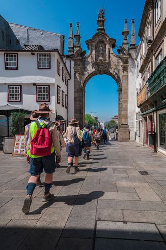 The scouts group walking under the historic arco da porta nova in Braga, Portugal, strolling along a sunny cobbled street through the old town.