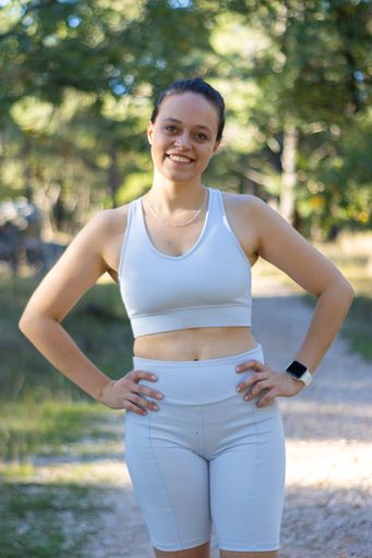 A vertical shot of a young Caucasian sporty woman smiling at the camera in nature wearing sports clothes.