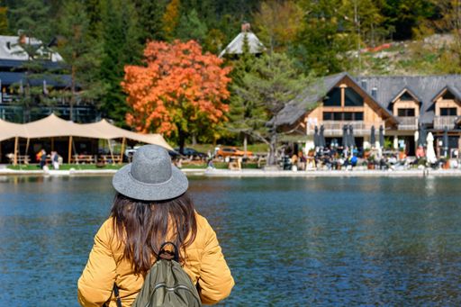 Rear view of woman standing on shore of lake, looking at beautiful tourist resort. Autumn nature around Lake jasna near Kranjska gora in Slovenia