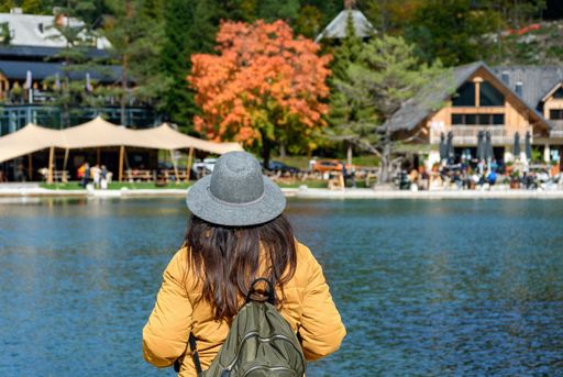 Rear view of woman standing on shore of lake, looking at beautiful tourist resort. Autumn nature around Lake jasna near Kranjska gora in Slovenia
