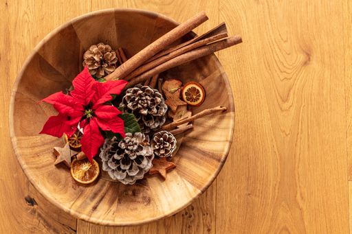 A wooden bowl full of cinnamon sticks, dried oranges, and cones for Christmas decoration