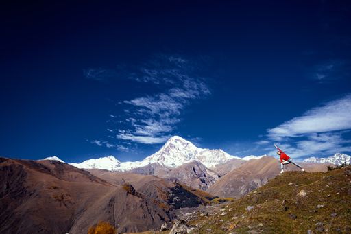 A person doing yoga on the grassy terrain with the Caucasus Mountains in the background