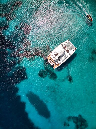 A bird's eye view of a white boat, swimming in the blue, shining sea under the sunlight