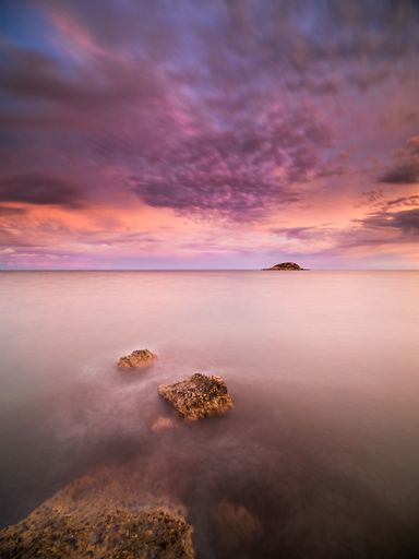 A vertical shot of the dramatic cloudy sky at sunset over the calm water in long exposure