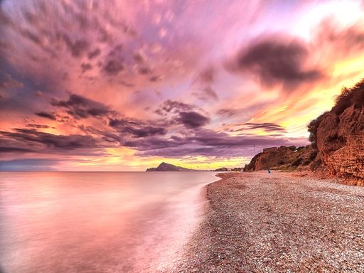 The dramatic cloudy sky at sunset over the coastal cliffs and calm water in long exposure