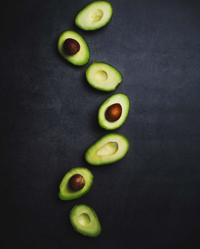 A vertical top view of half avocados in a wavy row on a black background
