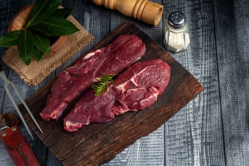A top view of raw striploin beef steaks with rosemary, bay leaves, salt, and  meat fork on the wooden table