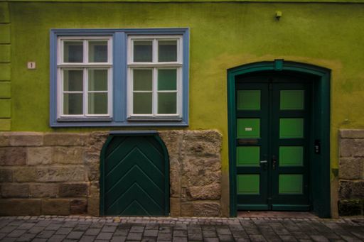 A old house entrance wooden door and blue windows on green facade