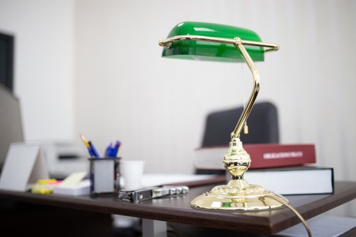 A closeup shot of a green desktop lamp at an office with books and files