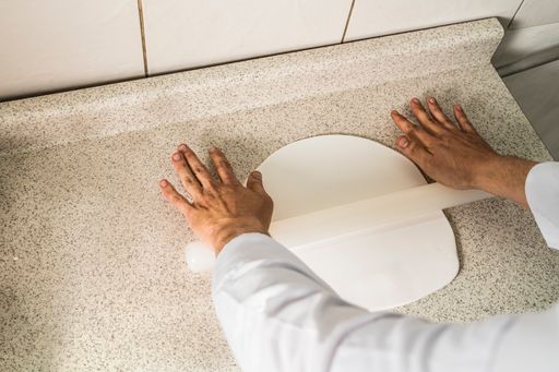 A top-view of a pastry chef kneading dough with a flat tool in a kitchen.