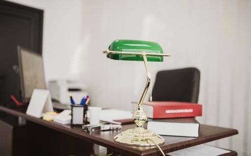 A closeup shot of a green desktop lamp at an office with books and files