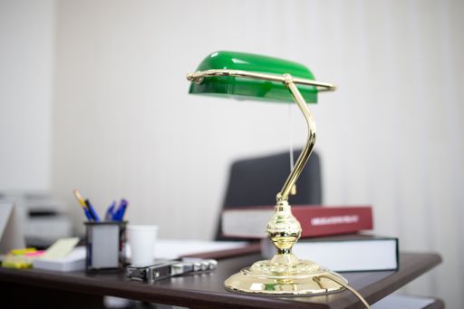 A closeup shot of a green desktop lamp at an office with books and files