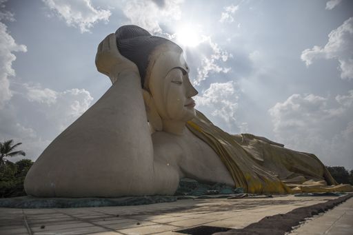 A closeup of the Mya Tha Lyaung reclining Buddha against a cloudy sky with a bright sun