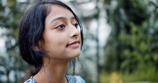 A candid shot of a pretty South Asian woman with a reserved smile while standing at a park