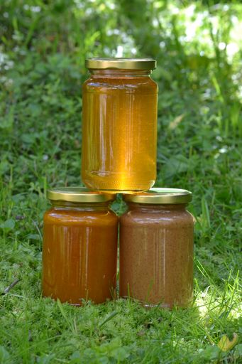 A vertical shot of three jars of fresh honey in a field