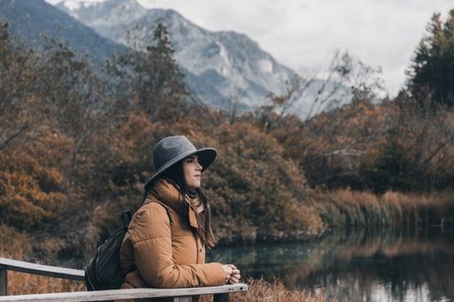 A young woman admiring beautiful autumn forest and a lake in Zelenci nature reserve, Slovenia.