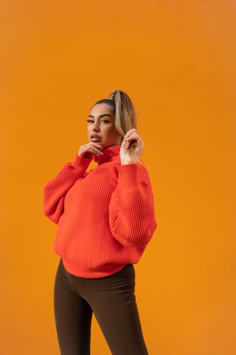 A fancy Spanish model in a bright casual outfit is standing in the bright orange studio background
