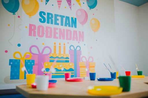 A birthday at a daycare center with colorful tableware on the wooden small tables 
Translation: Happy Birthday