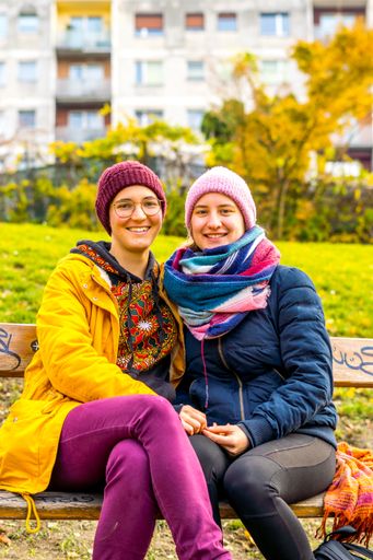 A vertical shot of a happy Caucasian lesbian couple in winterwear sitting on a wooden bench and smiling