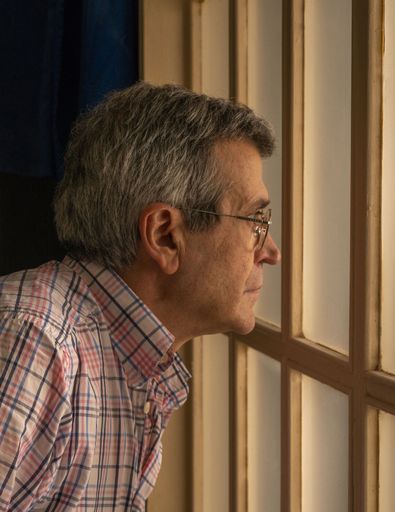 A vertical picture of an old man in glasses looking through the window