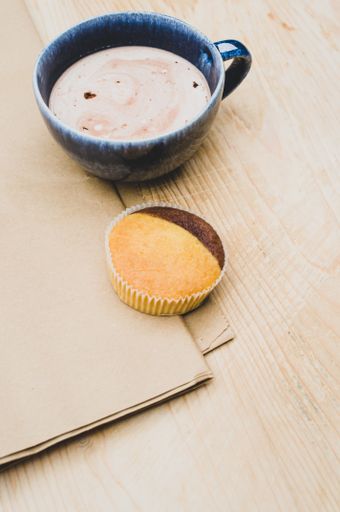 hot milk with cocoa in a blue cup and tasty cupcake on a rustic wooden and brown paper background