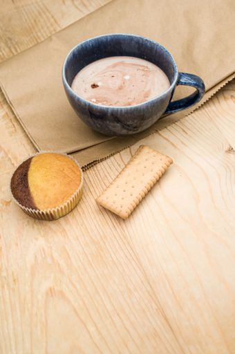hot milk with cocoa in a blue cup atasty cupcake and biscuits on a rustic wooden and brown paper background