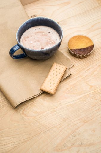 hot milk with cocoa in a blue cup atasty cupcake and biscuits on a rustic wooden and brown paper background