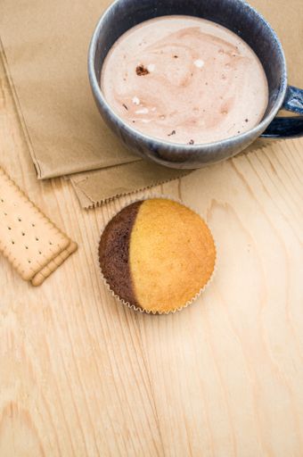 hot milk with cocoa in a blue cup atasty cupcake and biscuits on a rustic wooden and brown paper background