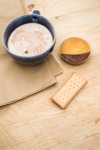 hot milk with cocoa in a blue cup atasty cupcake and biscuits on a rustic wooden and brown paper background