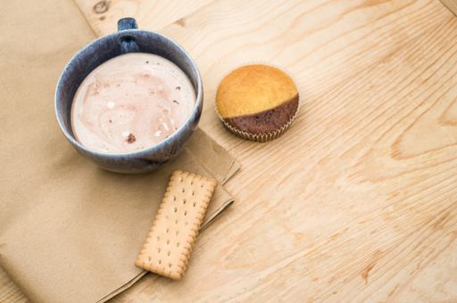 hot milk with cocoa in a blue cup atasty cupcake and biscuits on a rustic wooden and brown paper background