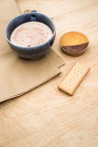 hot milk with cocoa in a blue cup atasty cupcake and biscuits on a rustic wooden and brown paper background
