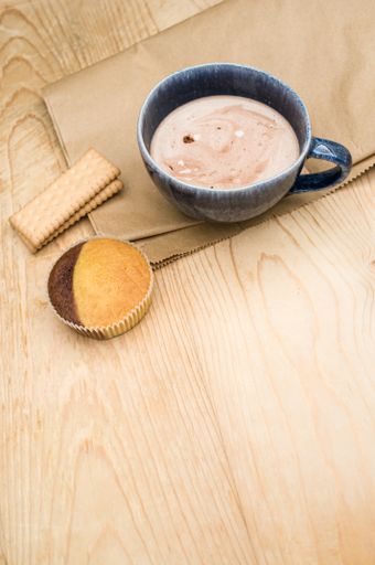 hot milk with cocoa in a blue cup atasty cupcake and biscuits on a rustic wooden and brown paper background